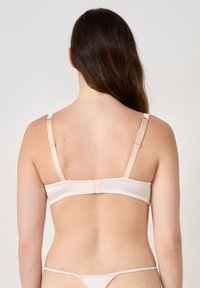 Beige bh met dunne verstelbare bandjes, een naadloze achterkant en haak-en-oogsluiting. Glad textuur met subtiele glans, ontworpen voor comfort.