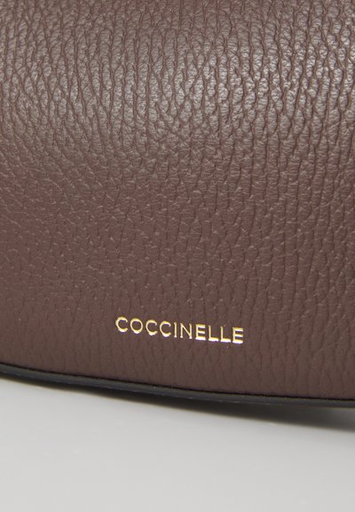 Sac à main en cuir texturé brun avec le logo doré "COCCINELLE". Présente une couture noire lisse à la base, mettant en valeur le design élégant.