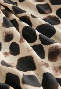 Tissu au motif de girafe présentant de grandes taches noires et brunes sur fond beige, avec une texture lisse et une apparence fluide.