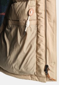 Beżowa kurtka puchowa z gładką podszewką, boczną kieszenią, sznurkiem ze skórzanym brązowym stoperem oraz czarnym zamkiem błyskawicznym.