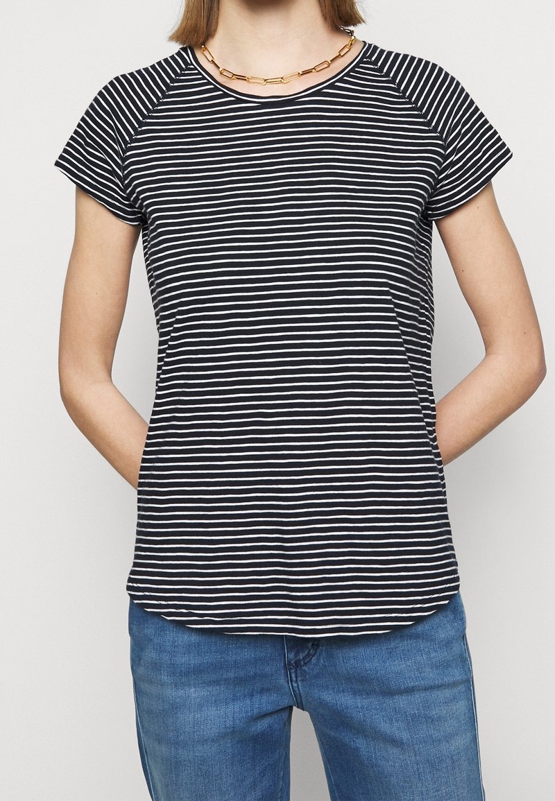 Svart och vit randig T-shirt med rund hals, korta raglansärmar, mjukt tyg och avslappnad passform. Bärs med blå jeans.