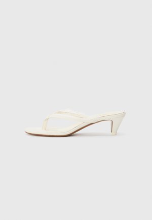 Sandales à talons blancs avec un design en T, présentant une texture douce et des détails subtils le long des sangles, un talon effilé et une semelle lisse.