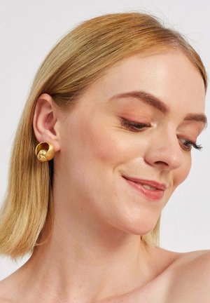 Gold metal earrings with a rounded design, featuring a smooth finish and a slight curve. The texture is polished and reflective.