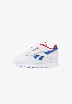 Witte Reebok-sneaker met blauwe en rode accenten, voorzien van één klittenbandsluiting en een dempende zool.