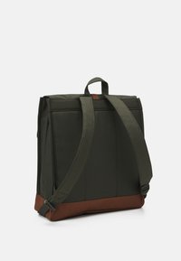 Zielony materiałowy plecak z brązowym dnem, płaska prostokątna forma, regulowane szelki, uchwyt na górze oraz minimalistyczny design.
