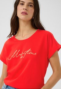 Tricou roșu cu mâneci scurte și un croi lejer. Prezintă un text brodat "Vibe-uri Maritime" din fir galben texturat. Material din bumbac neted.