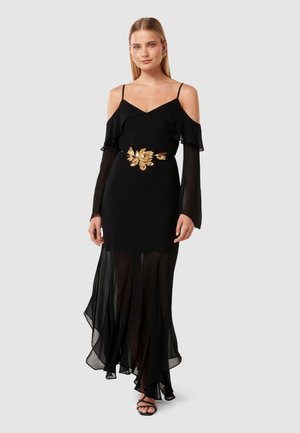 Black sheath dress with sheer, layered ruffles on sleeves and hem. Gold floral accent belt adds detail. Strappy black sandals complete the look.