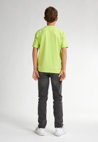 Camiseta de algodón verde lima de manga corta combinada con unos vaqueros gris oscuro y zapatillas blancas, vista desde atrás. Diseño simple, sin patrones.