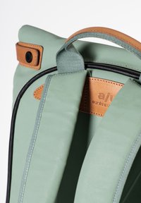 Grüner Stoff-Rucksack mit leichter Textur und Lederakzenten. Verfügt über einen Rollverschluss und ein auffälliges Markenlabel im Inneren.