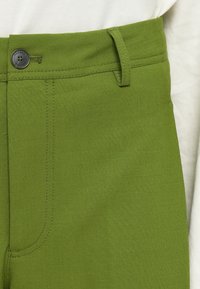 Zöld pamut keverék nadrág gombos zárással, övbújtatókkal és sima felülettel, látható varrás részletekkel.