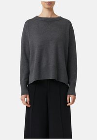Grauer Strickpullover mit Rundhalsausschnitt, gerippten Bündchen und einem leicht verkürzten, lockeren Schnitt. Kombiniert mit schwarzen weitem Hosen.