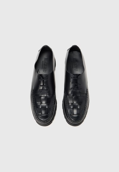 Zwarte leren schoenen met een geweven ontwerp op de neus, een glad bovenwerk, ronde veters en een contrasterende gestikte zoolrand.