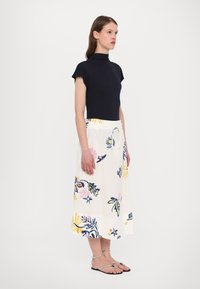 Navy mock neck top dengan lengan pendek dipadukan dengan rok midi berbahan putih bercorak bunga yang menampilkan cetakan berwarna-warni dan memiliki pinggang elastis.