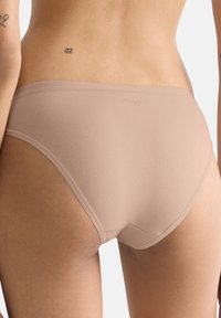 Mutandine beige in tessuto con texture liscia e design senza cuciture. Presentano un piccolo logo sulla fascia in vita. Assenza di motivi o accenti evidenti.