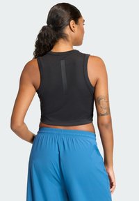 Svart cropped tanktop med et elegant design, med en vertikal detalj på baksiden. Kombinert med blå athletiske shorts.
