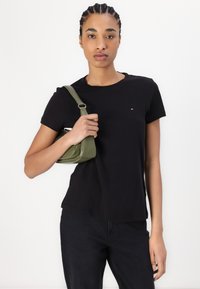 Svart crew-neck t-skjorte med et lite logo, kombinert med mørke jeans og en liten olivengrønn håndveske med skulderreim.