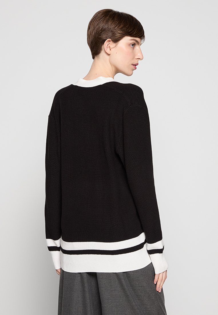 Un pull noir en tricot avec une texture côtelée, présentant un col blanc et des accents de rayures horizontales à l'ourlet et aux poignets.