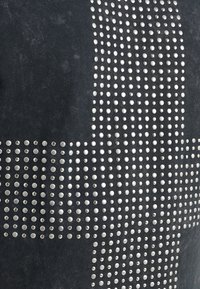 Haut en tissu noir avec des embellissements en clous métalliques disposés en motif quadrillé. La texture semble lisse avec un léger éclat.