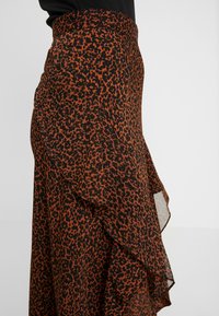 Jupe en imprimé léopard marron et noir avec un design fluide, dotée d'une ourlet volanté et d'une taille ajustée. Fabriquée en tissu léger.