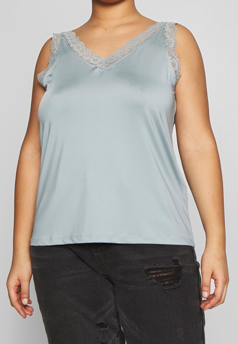 Ljusblå linne med V-ringning och spetsdetaljer på axelbanden. Mjuk, slät tyg; avslappnad design; matchad med slitna svarta jeans.