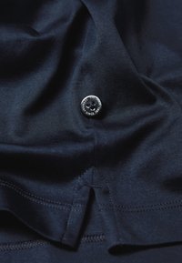 Marineblaues Tuch mit glatter Textur zeigt einen schwarzen Knopf, der mit "Van Laack 1881" markiert ist, am Boden mit sichtbarem Faden angenäht.