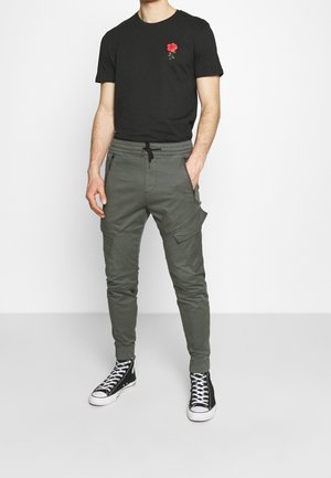 Sort t-shirt med rød rose broderi, parret med olivengrønne cargo-bukser med lynlåslommer og elastiske manchetter, afsluttet med sorte sneakers.