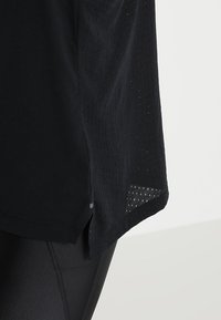 Czarna koszulka sportowa o luźnym kroju, z teksturowaną siateczkową wstawką u dołu oraz zaokrąglonym brzegiem z bocznymi rozcięciami.