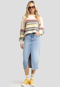 Pull en tricot épais de couleur crème avec des rayures multicolores ; jupe en denim bleu clair taille haute avec fente devant ; baskets jaunes avec des chaussettes blanches.