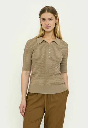 Polo en maille côtelée beige avec manches courtes et col. Doté d'une patte de boutonnage avec quatre boutons. Porté avec un pantalon marron taille haute.