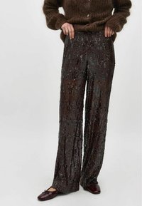 Pantaloni largi cu paiete, de culoare maro închis, cu o suprafață texturată și paiete strălucitoare, asortați cu un pulover lejer din tricot maro.