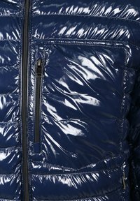 Marineblauwe pufferjack met een glanzende, gestikte textuur, voorzien van een ritszak aan de voorkant en zwarte ritsdetails op de sluiting.