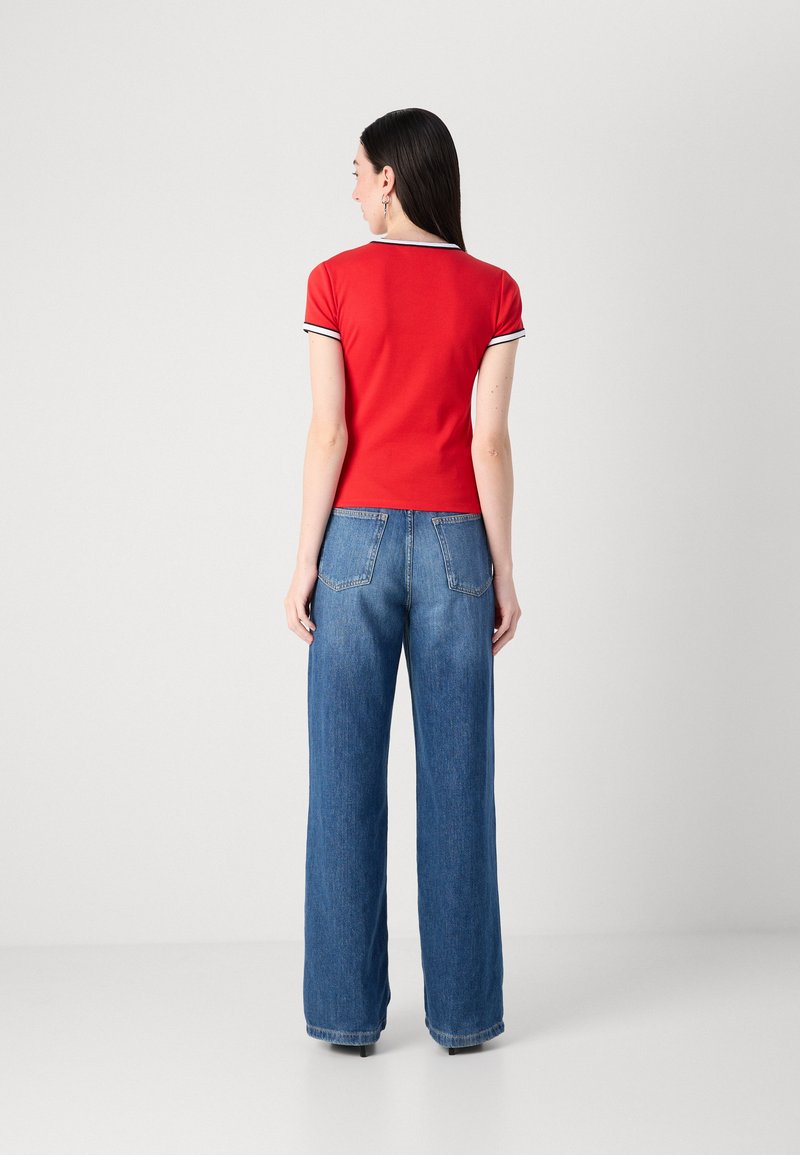 Top corto rojo de manga corta con un cuello a rayas en blanco y negro, combinado con unos pantalones vaqueros de pierna ancha en denim azul que cuentan con dos bolsillos traseros.