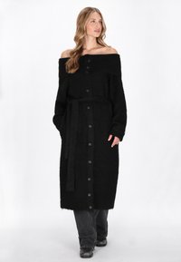 Cardigan negru, cu umeri descoperiți, confecționat dintr-un material pufos, având un închidere cu butoane pe față, cordon la talie și mâneci lungi cu manșete cu un model de pliuri.