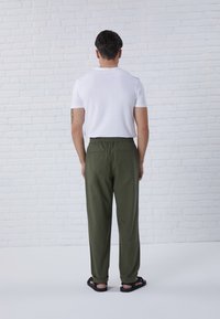 Pantaloni verdi con vita elastica e taglio rilassato, dotati di due tasche posteriori, abbinati a una maglietta bianca a maniche corte e sandali neri.