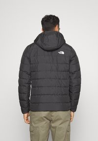 Svart puffjacka med huva, med quiltat mönster och The North Face-logotypen på baksidan. Slät tyg, lätt och isolerad.