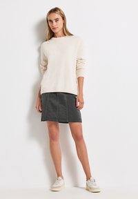Sweater tricoté beige clair avec des poignets côtelés associé à une jupe gris foncé. La tenue est complétée par des baskets blanches.