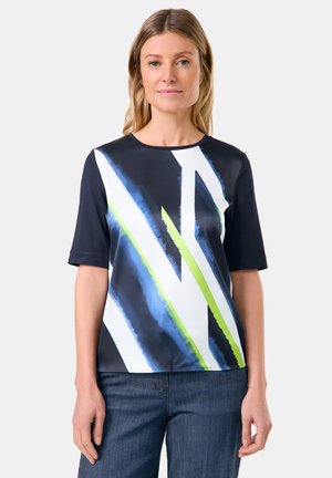 Kurze Ärmelbluse in Marineblau mit geometrischem Design in Blau und Neon-Grün. Glatte Textur mit Rundhalsausschnitt. Kombination mit Denim.