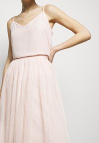 Camisole en soie rose clair avec des bretelles fines associé à une jupe en tulle à pois, créant une silhouette fluide et superposée.