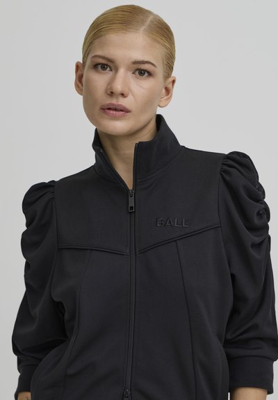 Crna jakna na patentni zatvarač s naduvanim rukavima, mekane tkanine i reljefnim logotipom "BALL" na prsima; ima visok ovratnik i bočne džepove.