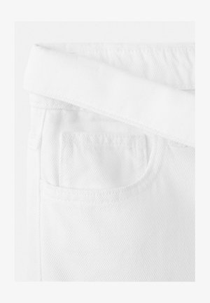 Detail horní části bílých džínsů z denimu, zobrazující složený pas a přední kapsu s viditelným šitím.