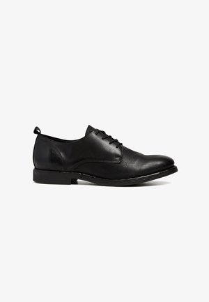 Chaussure Oxford en cuir noir avec un laçage fermé, un petit talon, un bout arrondi et une languette à l'arrière, présentée en profil latéral sur fond blanc.