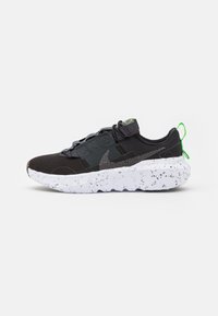 Black athletic shoe with a textured mesh upper, gray accent panels, and a white speckled sole. Features green pull tab and laces.
