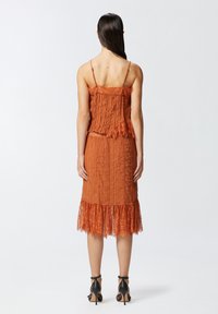 Haljina u rustično narančastoj boji s nabranim detaljima i čipkastim rubom. Podesive tanke naramenice i široki kroj stvaraju suptilnu dimenziju i teksturu.