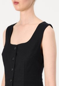 Zwarte mouwloze jurk met een vierkante halslijn, voorzien van een knoopdetail aan de voorkant en een gestructureerde pasvorm. Glad stoftextuur.