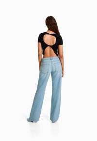 Black ribbed short-sleeve top with cutout back; paired with light blue high-waisted wide-leg jeans. Casual fabric and design details visible.