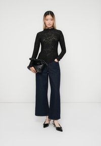 Body em renda preta de mangas longas com padrão floral, combinado com jeans escuros de cintura alta e perna larga e sapatos pretos de salto. Bolsa de mão preta.