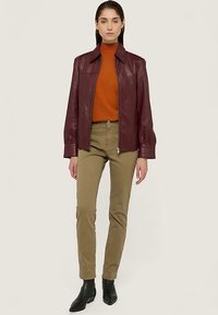 Vinröd läderjacka med hög krage, kombinerad med en orange polotröja, olivgröna byxor och svarta ankelboots. Mjuk textur, figurnära design.