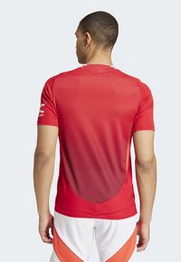 Maillot de sport rouge avec un design dégradé, à manches courtes et en tissu texturé. Le dos comporte un détail en coupure courbée.