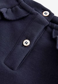 Temno modra bombažna srajca z rebrastim ovratnikom, ki ima gumbasto zapiranje in nabran detajl ob robu ovratnika.