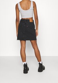 Černá džínová sukně s rozparkem, vybavená zadními kapsami a koženou nálabelkou. Vytvořena v kombinaci se šedým zkráceným topem a černými kotníkovými botami.